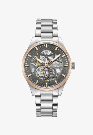 Szkieletowy zegarek automatyczny z srebrną bransoletą ze stali nierdzewnej, szarym cyferblatem z złotymi akcentami oraz odkrytymi detalami mechanizmu.