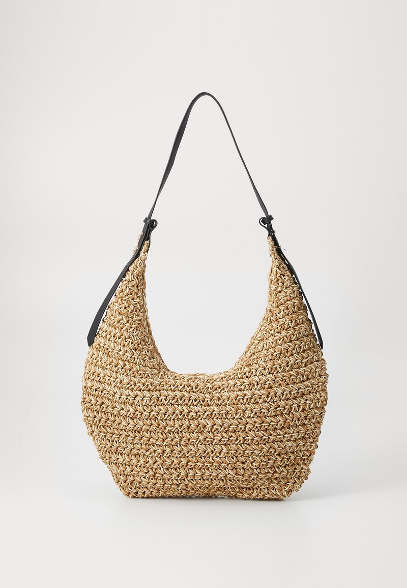 Geflochtene Strohtasche mit abgerundeter Silhouette, ausgestattet mit einem schwarzen Leder-Schultergurt. Texturierte, natürliche Oberfläche und leichtes Design.