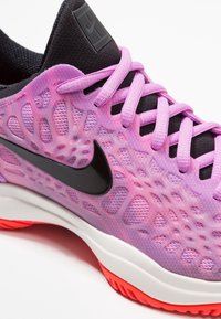 Nike träningsskor med en lila nätöverdel med en texturerad mönster, svarta accenter, rosa snören och en vit mellansula med röd yttersula.