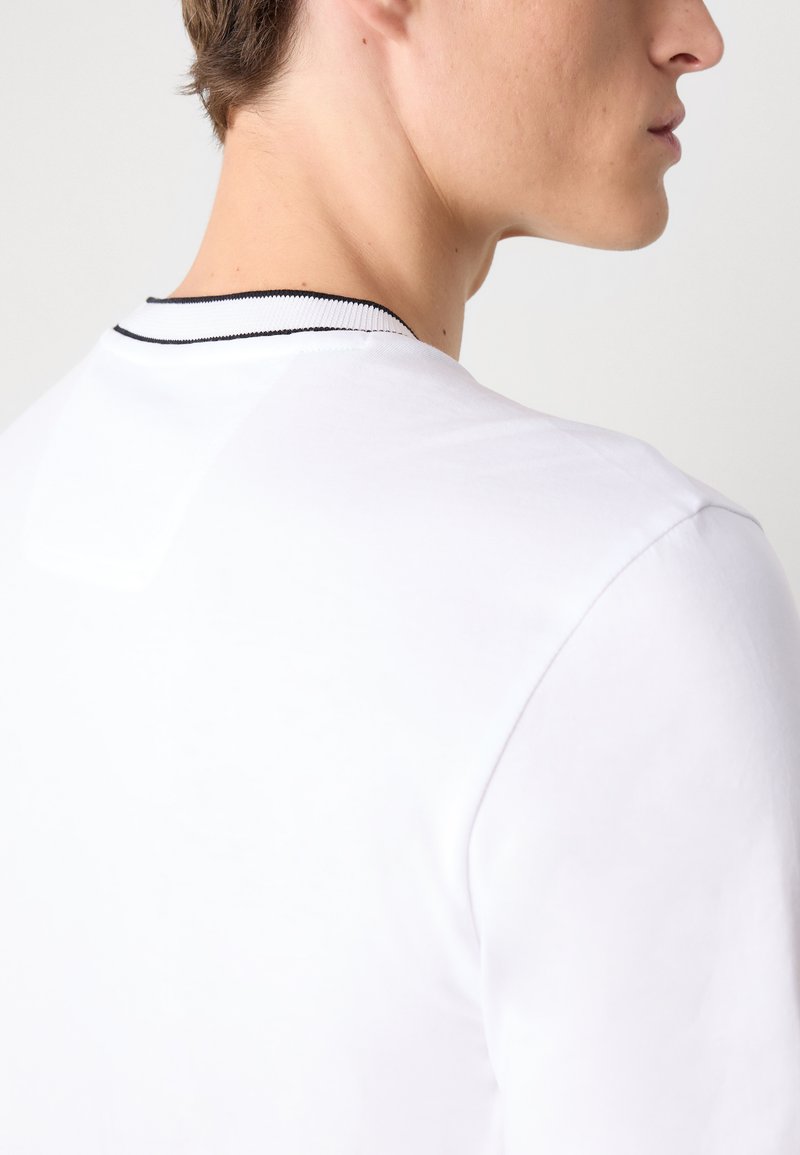 Weißes kurzärmliges Hemd mit einem gerippten Kragen in Schwarz. Glattes Material mit klassischer Passform, das einfache, klare Linien zeigt.