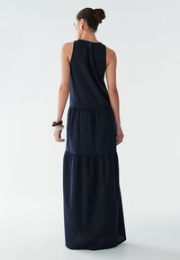Námořnicky modré šaty s vrstevnatým střihem, s nařaseným výstřihem a splývavým spodním lemem. Hladká textura, minimalistický design a bez viditelných vzorů.