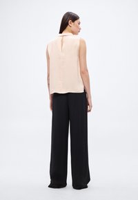 Svetloružová blúzka bez rukávov s detailom v tvare kľúčovej dierky na chrbte, skombinovaná s čiernymi širokými nohavicami, vyrobená z mäkkej látky.