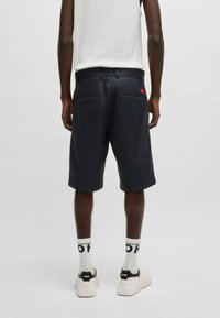 Marinblå shorts med avslappnad passform, som har två bakfickor med knappar, elastisk midja och en liten röd logotypetikett.
