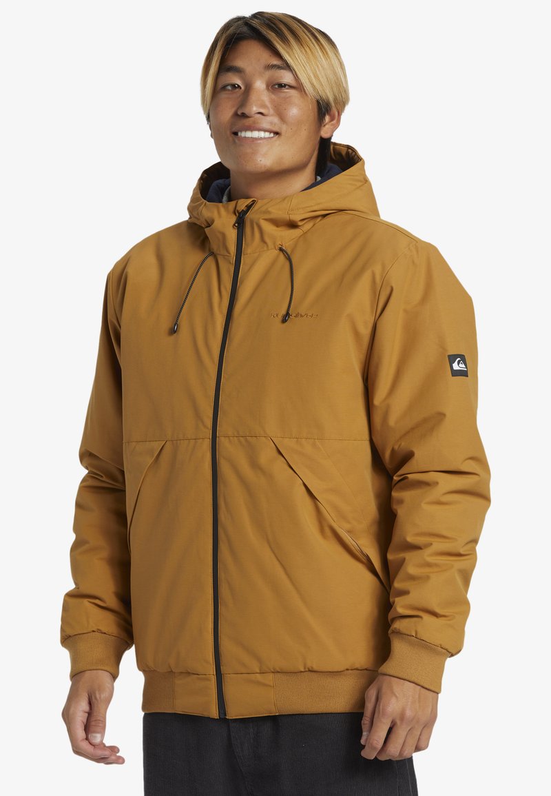Chaqueta con capucha naranja, con cremallera frontal y dos bolsillos laterales. Presenta un logo de Quiksilver en la manga y puños elásticos.