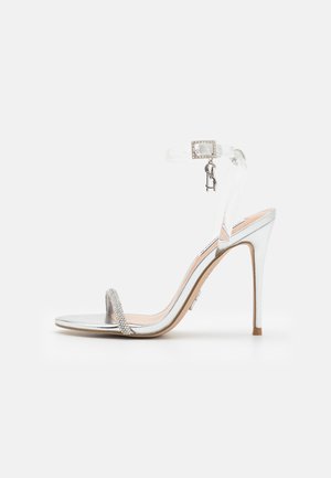 Sølvfarvet sandal med høje hæle, metallisk finish, klar ankelrem og rhinsten-detaljer på tå-remmen. Klassisk åben tå-design.