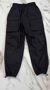 Svarta cargobyxor tillverkade av lätt material med resårmidja, flera sidofickor och elastiska fållar. Slät textur.