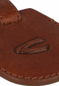 Sandale en cuir marron avec une surface texturée, présentant une forme courbée et des bords surpiqués. Logo embossé sur la partie supérieure.