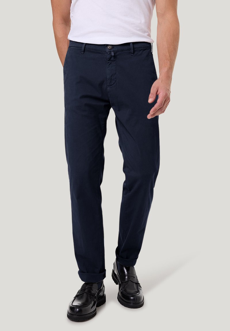Marineblaue Baumwollchinos mit geradem Schnitt, Gürtelschlaufen und hochgekrempelten Säumen, kombiniert mit schwarzen Schuhen und einem weißen T-Shirt.