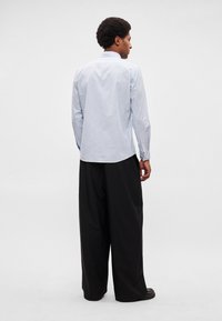 Ανοιχτό μπλε πουκάμισο με μακριά μανίκια, κουμπιά και διακριτικό καρό σχέδιο, με καμπυλωτό τελείωμα, σε συνδυασμό με μαύρο παντελόνι με φαρδιά μπατζάκια.