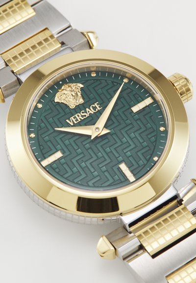Auksinė ir sidabrinė apyrankė su žalia raštuota ciferblatu, kuriame matomas Versace logotipas, auksinės rodyklės ir tekstūruoti metaliniai akcentai.