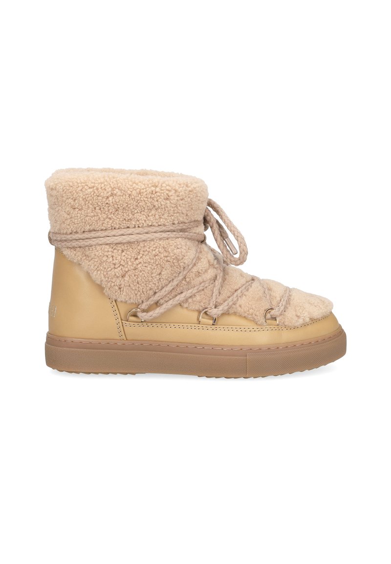 Bottines beige avec un dessus en shearling doux, fermeture à lacets et semelle en caoutchouc beige, conçues pour le confort et la chaleur.