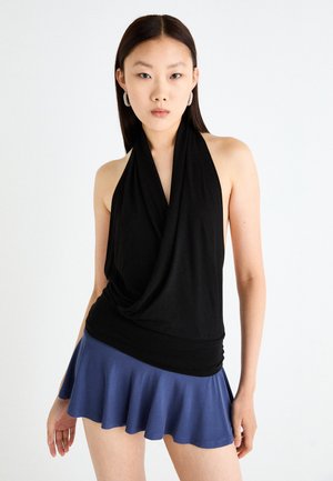 Svart halterneck topp med drapert halslinning, sammen med et vidt dypblått skjørt. Stoffet virker glatt med en lett tekstur som fremhever bevegelse.