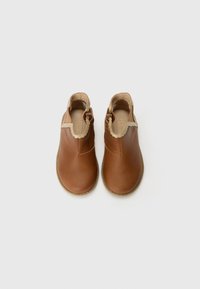 Bottes ankle en cuir marron avec un bout arrondi, un bord beige à motifs festonnés et un détail de boucle sur le côté. Semelle en caoutchouc plate.