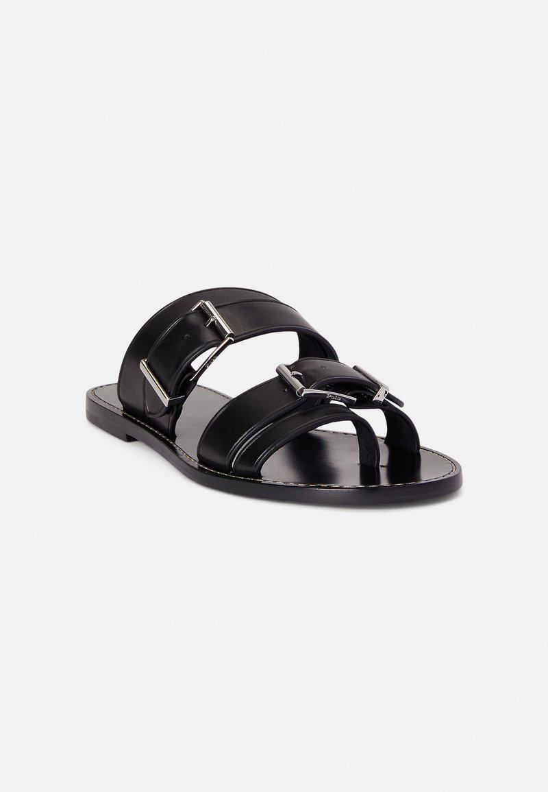 Black leather sandals featuring wide straps with metallic accents, flat sole, and open toe design. Smooth texture with subtle stitching detail.