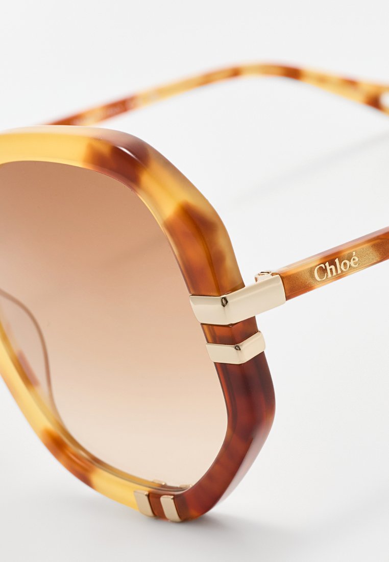 Lebhafte Schildpatt-Sonnenbrille mit übergroßen sechseckigen Gläsern, die einen sanften Farbverlauf aufweisen, und goldfarbene Metallakzente an den Scharnieren.