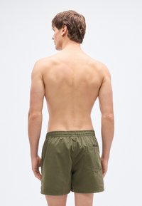 Πράσινα μαγιό βερμούδα ελιάς με ελαστική μέση, διαθέτει πίσω τσέπη  και μικρό ταμπελάκι με λογότυπο. Λείο ύφασμα, μήκος πάνω από το γόνατο.