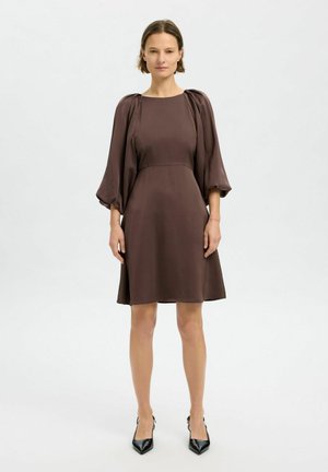 Vestido marrón de longitud a la rodilla con una textura suave y sedosa. Presenta mangas abullonadas y un corpiño ajustado. Combinado con tacones negros de punta.