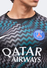 Κοντινή λήψη κορμού που φοράει φανέλα της Paris Saint-Germain με μαύρο και μπλε ζιγκ-ζαγκ σχέδιο, με το λογότυπο του χορηγού Qatar Airways και το σήμα Nike.
