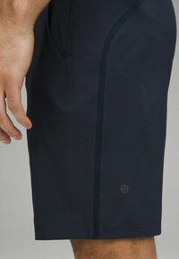 Navy athletic shorts made from lightweight fabric, featuring a streamlined design, side pocket, and logo detail near the hem.