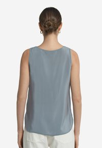Ärmlös topp i mjukt, ljusblått tyg. Har en rund halsringning och en slät yta med rundad nederkant. Inga synliga mönster eller dekorationer.