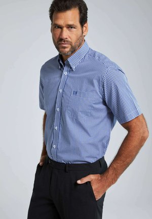 Camisa de manga corta, abotonada, en un patrón de cuadros azul y blanco, con cuello, bolsillo en el pecho y un ajuste relajado. Combinada con pantalones negros.