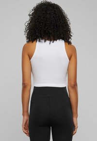Witte cropped tanktop met een ronde halslijn, gecombineerd met hoge zwarte leggings. De top heeft een aansluitend ontwerp en een mouwloos model.