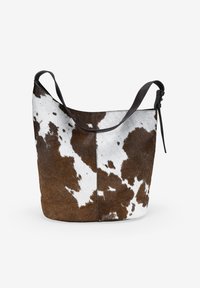 Bolso de piel de vaca marrón y blanco con forma holgada, que cuenta con una sola correa para el hombro y un acento de cuero cerca de la abertura.