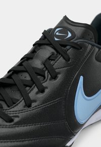 Μαύρο αθλητικό παπούτσι με ανάγλυφο δερμάτινο πάνω μέρος, μαύρα κορδόνια και λογότυπο Nike σε γαλάζιο χρώμα. Διαθέτει ραφές και μαξιλαρωμένο γιακά.