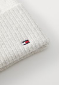 Rillede kremfargede strikkede luer med logomerke som har røde, hvite og blå striper. Myk tekstur, allsidig design, egnet for kaldt vær.