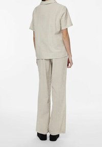 Striped two-piece loungewear set in beige and white. Short-sleeve top and loose-fitting trousers with a lightweight, textured fabric.