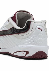 Witte sportieve schoen met kastanjebruine accenten, voorzien van een gestructureerde bovenkant, glad synthetisch materiaal, gebogen vorm en een kenmerkend logo.