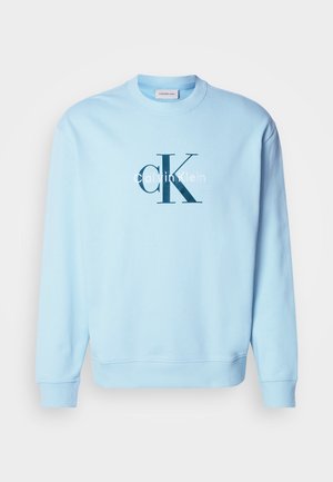 Šviesiai mėlyna medvilnės mišinio džemperis, su apvaliu kaklu ir raukšlėmis ant rankovių. Priekyje dideliu tamsiai mėlynu šriftu pavaizduotas "Calvin Klein" logotipas.