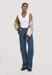 Witte v-hals tanktop onder een oversized, veelkleurige gebreide cardigan. Wijde blauwe jeans met een trekkoord en bruine schoenen.