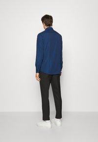 Marinblå långärmad skjorta med ett subtilt mönster, kombinerad med mörka byxor och vita sneakers. Skjortan har en klassisk krage och knäppte ärmslut.