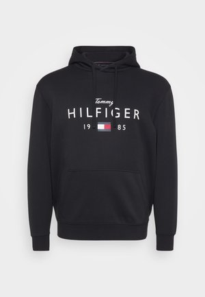 Black hoodie made of soft cotton blend, featuring a front pouch pocket, drawstring hood, and bold white "Tommy HILFIGER 1985" logo.