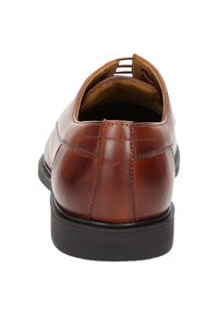 Scarpe slip-on in pelle marrone con punta arrotondata, cuciture visibili e suola in gomma nera a contrasto. Design aperto sul retro per un facile utilizzo.