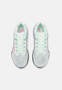 Buty do biegania Nike z białą siateczkową cholewką, miętowozielonymi akcentami, czarną podeszwą i różowym logo; posiadają teksturowaną tkaninę z małymi otworami wentylacyjnymi.