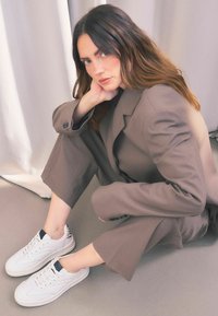 Blazer beige oversized et pantalon large assorti, associés à des baskets blanches avec un talon texturé. Tissu doux et lisse et design moderne.