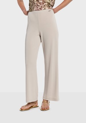 Lyse beige bukser med vide ben i blødt stof, med høj talje og diskret logo i siden, stylet med flade gyldne sandaler.