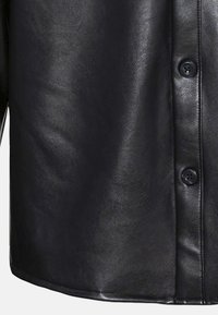 Czarna skórzana koszula o gładkiej teksturze, z zapięciem na guziki z przodu i zaokrąglonym dołem. Zawiera czarne guziki i subtelny połysk.