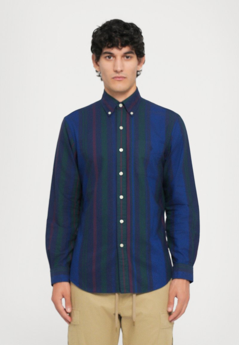 Camisa de botones en azul marino con rayas verticales en verde y marrón, de manga larga y botones blancos, hecha de una tela suave.