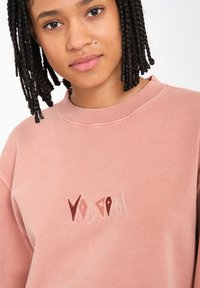 Rosa Sweatshirt mit geripptem Kragen, versehen mit gesticktem "Volcom" in kontrastierenden Farbtönen. Weicher Stoff und lockere Passform.