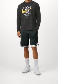 Long-sleeve black Nike shirt with white and yellow text, paired with dark green shorts featuring white stripes and a Nike logo on the hem.