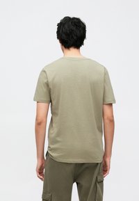 Λαδί πράσινο μπλουζάκι με στρογγυλή λαιμόκοψη από απαλό ύφασμα. Διαθέτει κοντά μανίκια και άνετη εφαρμογή, με απλό σχέδιο και χωρίς ορατά λογότυπα.