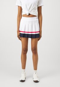 Gonna da tennis bianca a pieghe con strisce rosse e blu navy, vita elasticizzata e texture del tessuto liscia. Abbinata a scarpe da ginnastica bianche.
