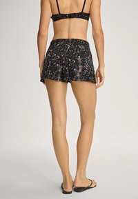 Černé šortky s hadím vzorem, vyrobené z lehké tkaniny. Elastický pas, délka do poloviny stehna, kombinované s černými žabkami.