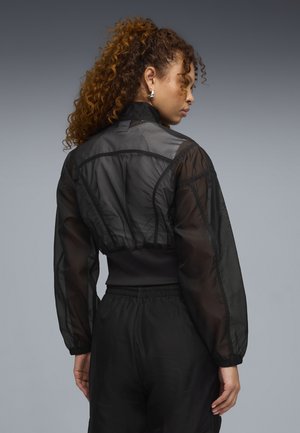 Musta lyhyt takki, valmistettu läpikuultavasta materiaalista, jossa on pussihihat, korkea kaulus ja joustava vyötärönauha. Yhdistetty vastaaviin housuihin.