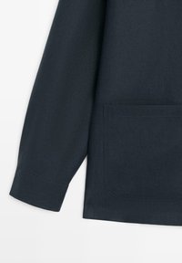 Mørk marineblå langærmet skjorte med opsmøgede ærmer og en stor rektangulær lomme på den nederste forside.