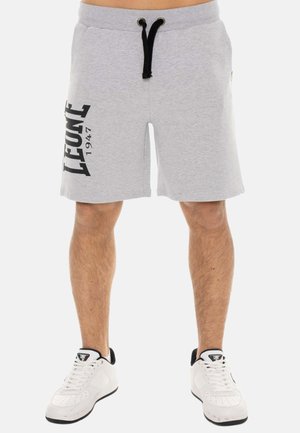 Homme portant un short gris clair avec un cordon noir et le texte ""LEONE 1947"" sur la jambe gauche, et des baskets blanches avec des détails noirs.