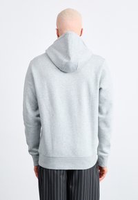 Gray hoodie with a large, structured hood, soft texture, ribbed cuffs and hem, and minimalistic design. Worn with striped black pants.
